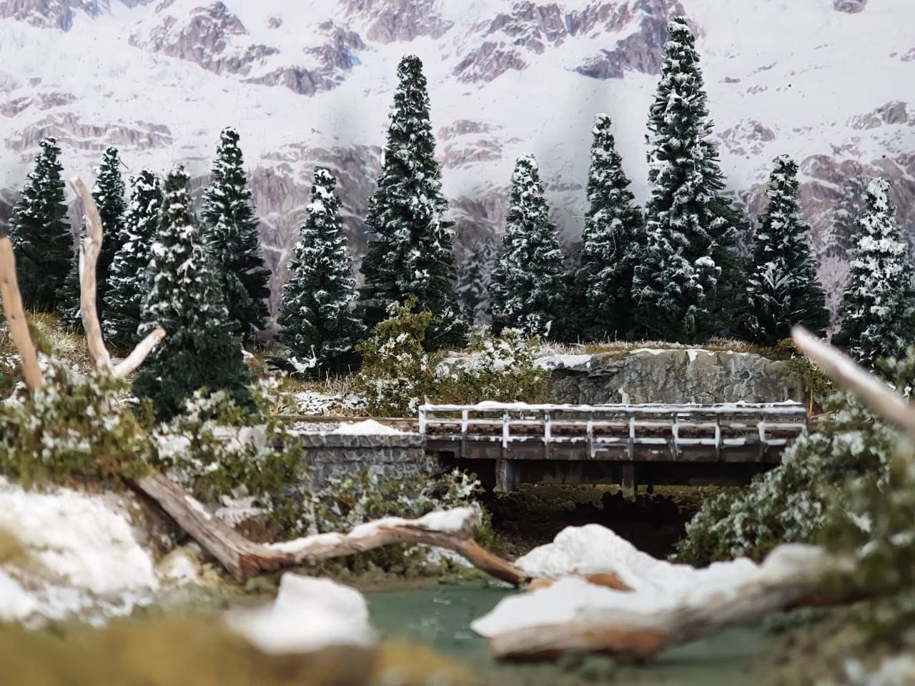 Ponte ferroviária em diorama nevado LVL Artes, cadeia de montanhas ao fundo